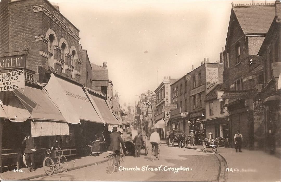 Old photo of a high street with horses, carts, and bicycles
