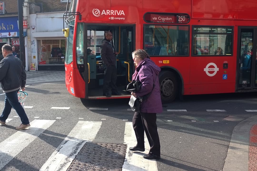 Photo of a lady crossing a road while a bus waits for traffic to clear